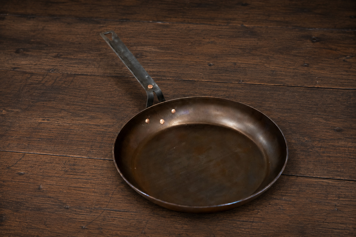 Texas Pan Company 11-inch carbon steel skillet with copper-riveted handle on a wooden farmhouse table