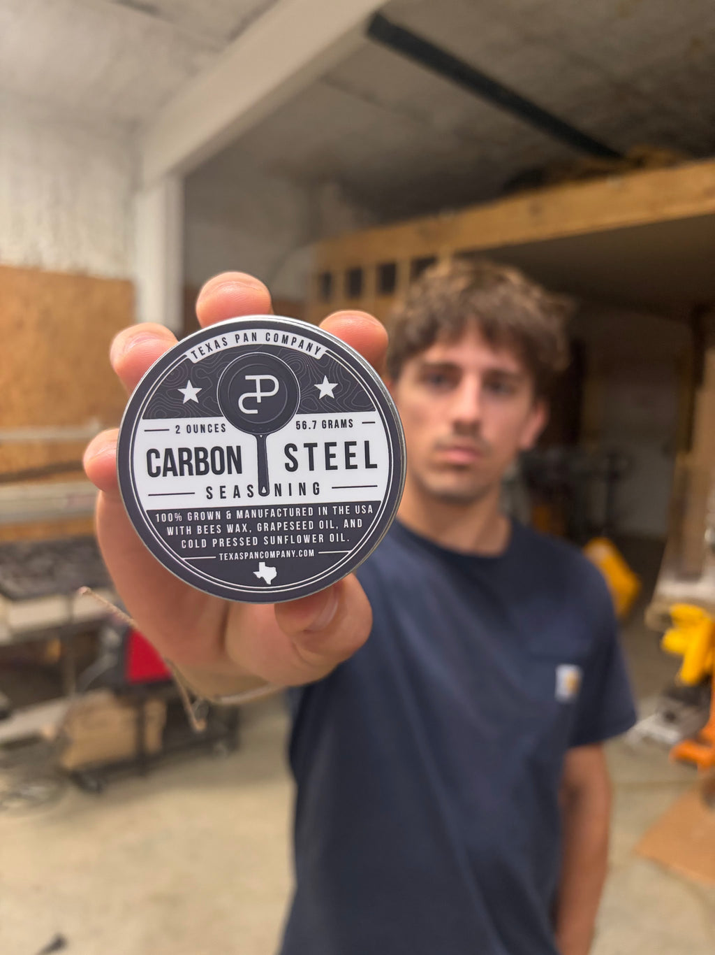 A hand holding the Carbon Steel Seasoning tin in the shop