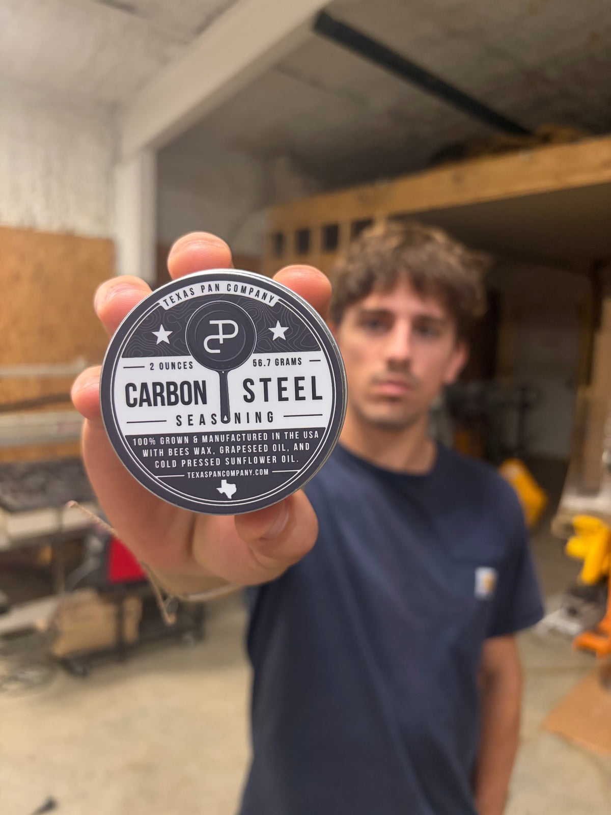 A hand holding the Carbon Steel Seasoning tin in the shop