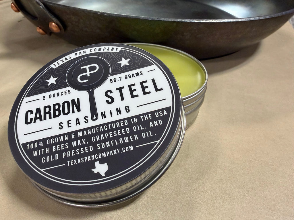Open Carbon Steel Seasoning tin with the lid leaning against it and a skillet behind