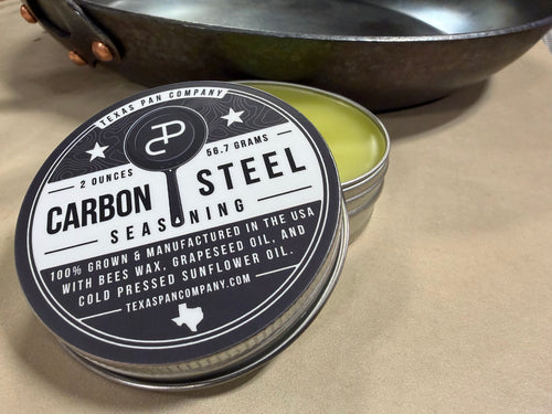 Open Carbon Steel Seasoning tin with the lid leaning against it and a skillet behind