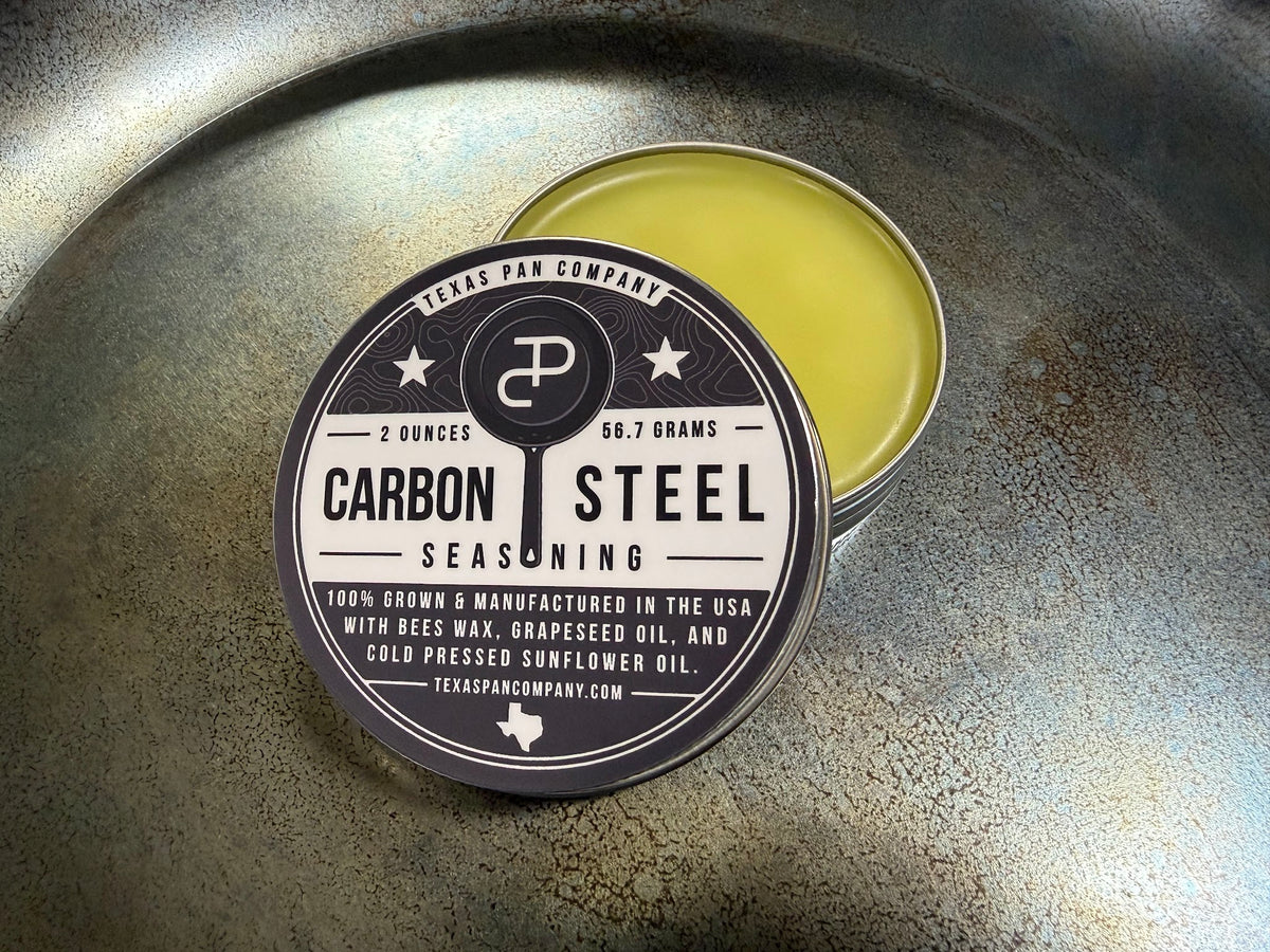 Open Carbon Steel Seasoning tin resting in a carbon steel skillet, balm showing