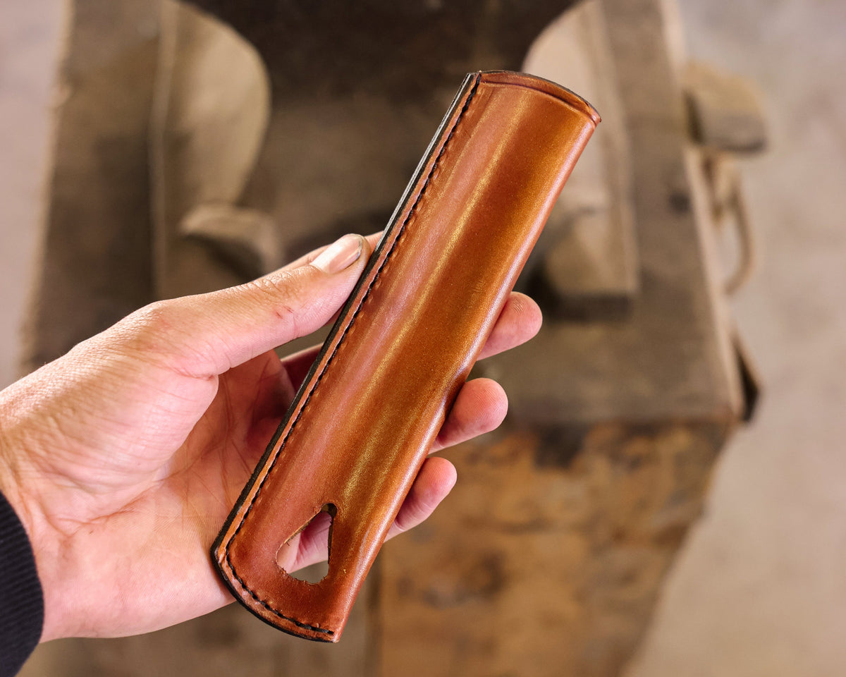 A hand holding the Leather Handle Cover, tan full grain leather with stitched edges and a hanging hole