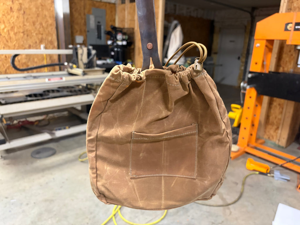 Canvas Skillet Bag in tan waxed canvas with The Original's handle coming out the drawstring top, hanging in the Texas Pan Company shop