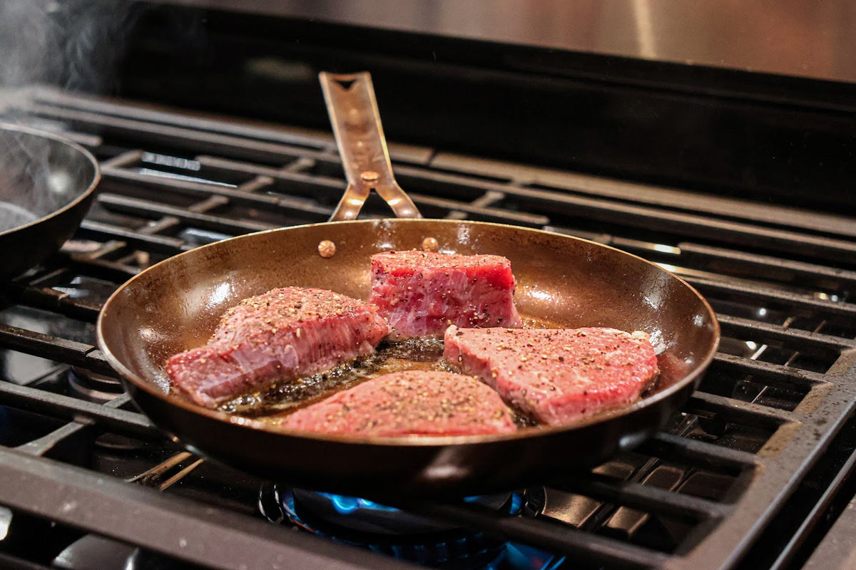 Four steaks searing in The Original carbon steel skillet on a gas burner