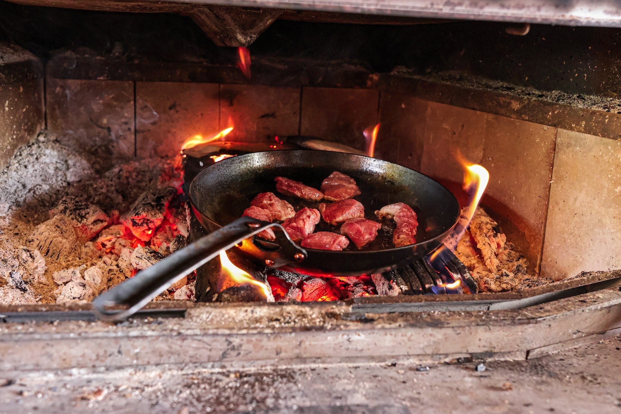 The Original carbon steel skillet searing steak on the coals of a wood fire