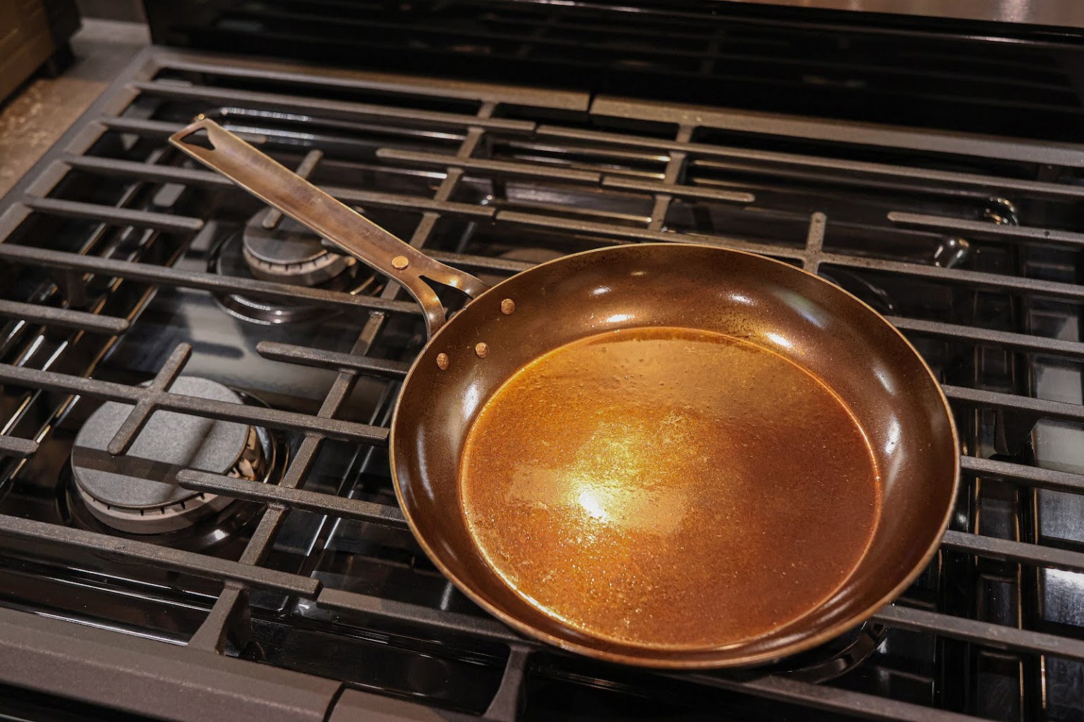 The Original carbon steel skillet on a gas range with its steel handle and copper rivets